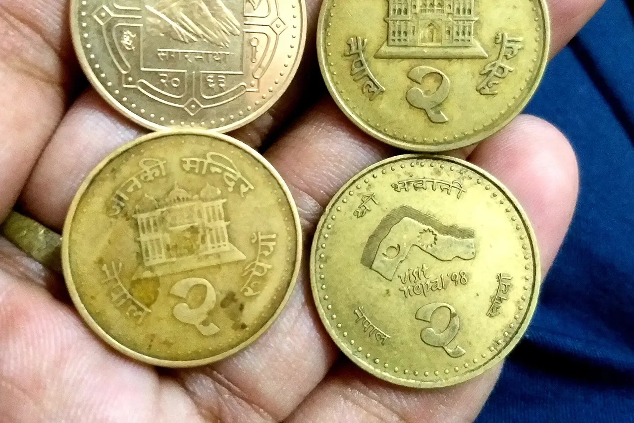 Four brass Nepali two-rupee coins held in an open hand