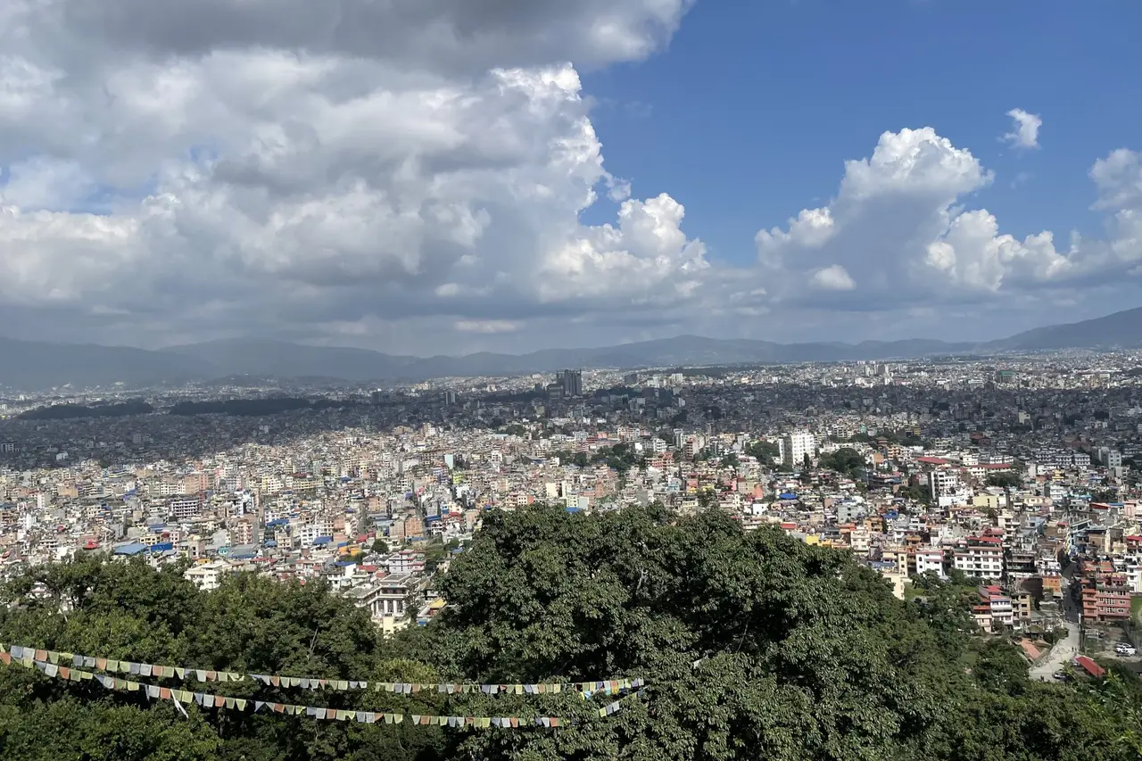 A dense city of low buildings spreading to the hills under a cloudy sky